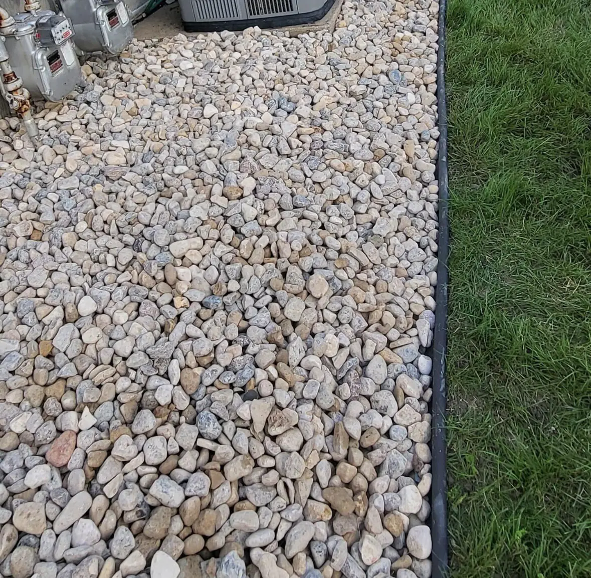 Clean river rock landscaping bed beside healthy grass